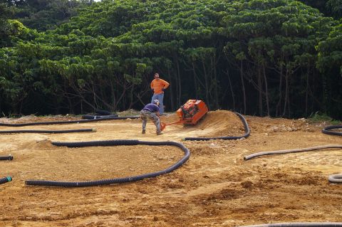 1986 Ford Bronco - Two people work on constructing an RC track, using a compactor on a dirt mound surrounded by black tubing.