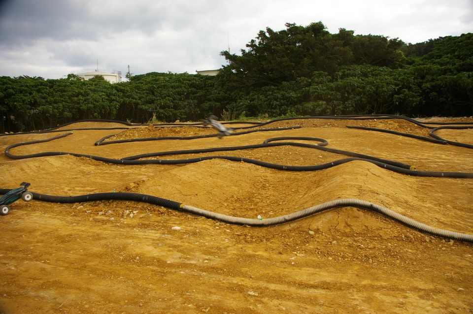 RC track with dirt mounds and black tubing, two remote-controlled cars visible