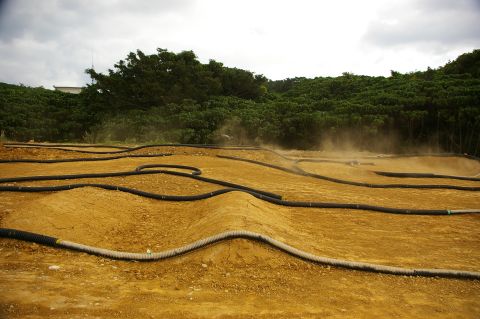 1986 Ford Bronco - RC car track with dirt mounds and black hose borders under a cloudy sky.