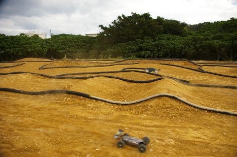 1986 Ford Bronco - Remote control cars navigate a challenging dirt track with multiple obstacles and turns.