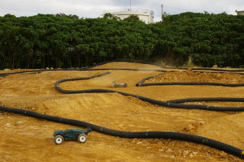 1986 Ford Bronco - Remote control cars navigate a dusty dirt track with black tubing defining the course.