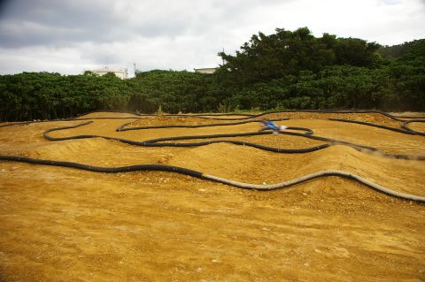 1986 Ford Bronco - A radio-controlled car navigates a winding dirt track with berms and jumps.
