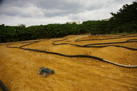 1986 Ford Bronco - Remote control cars race on a dirt track with a cloudy sky overhead.