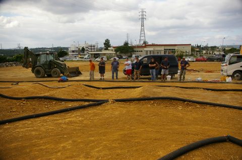 1986 Ford Bronco - A group of people observe an RC track with various vehicles and equipment present under a cloudy sky.