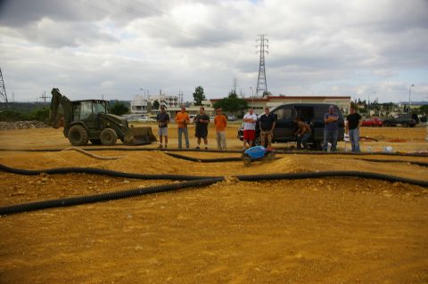 1986 Ford Bronco - Men gather around a dirt track to watch remote control cars race, with a backhoe and van nearby.