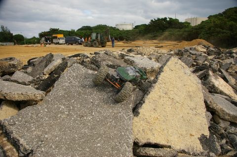 1986 Ford Bronco - A green remote control rock crawler navigates a pile of broken asphalt on a construction site.