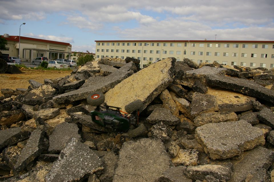 Green remote control car tipped over on a pile of broken asphalt