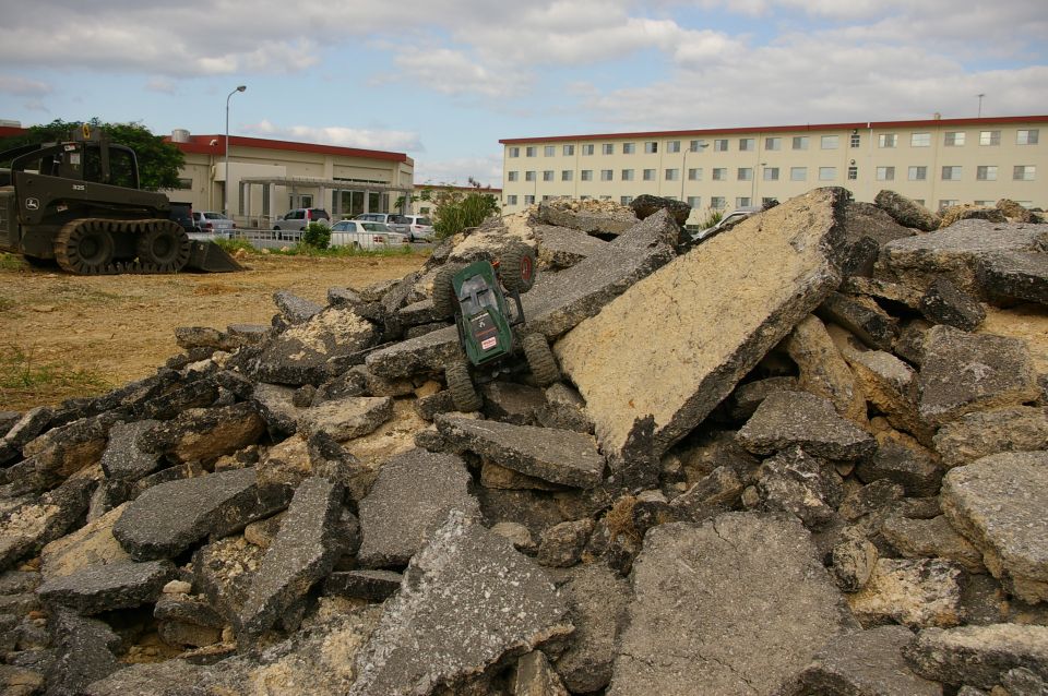 green remote control car on pile of broken asphalt with buildings in background