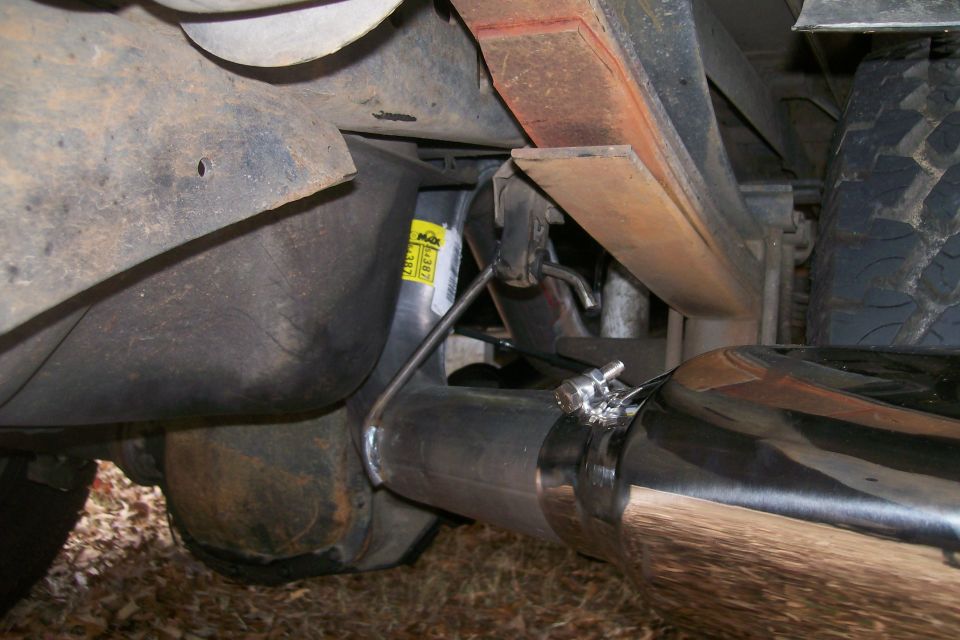 Close-up of a shiny exhaust pipe clamped to a larger pipe, with a leaf spring and part of a tire visible above
