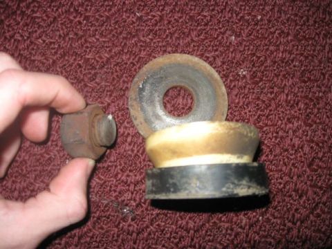 1992 Ford Bronco - Close-up of automotive suspension components, including a bolt, bump stop, and washer, resting on a textured surface.