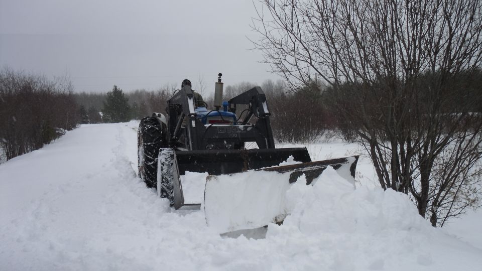 Tractor with a front plow pushing snow on a snowy day
