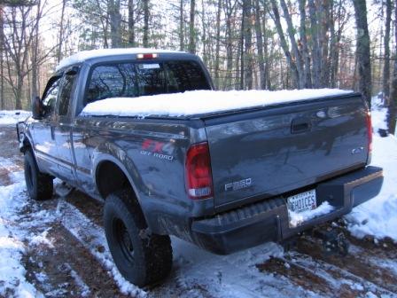 2003 Ford F-350 - Rear view of a 2003 Ford F-350 pickup truck covered in snow, parked in a wooded area.