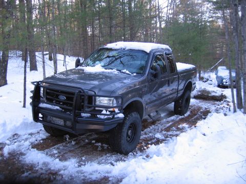 2003 Ford F-350 - A Ford F-350 sits in a snowy wooded area, with another vehicle covered in a tarp in the background.