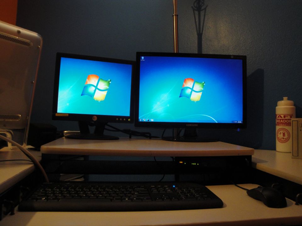 Two computer monitors displaying Windows 7 wallpaper, a keyboard, and a mouse on a desk