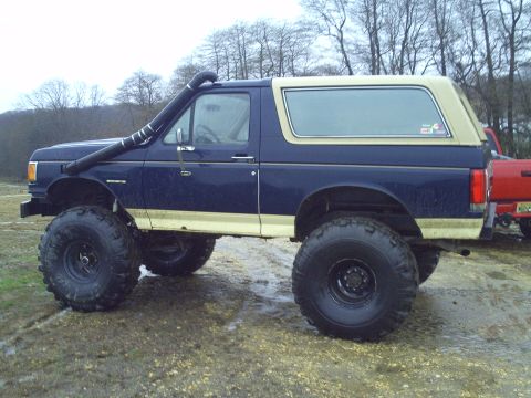 1990 Ford Bronco - This lifted Ford Bronco features a snorkel and is parked on a muddy surface next to another vehicle.