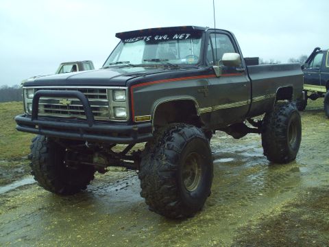 1990 Ford Bronco - A heavily modified pickup truck with oversized tires sits in a muddy field.