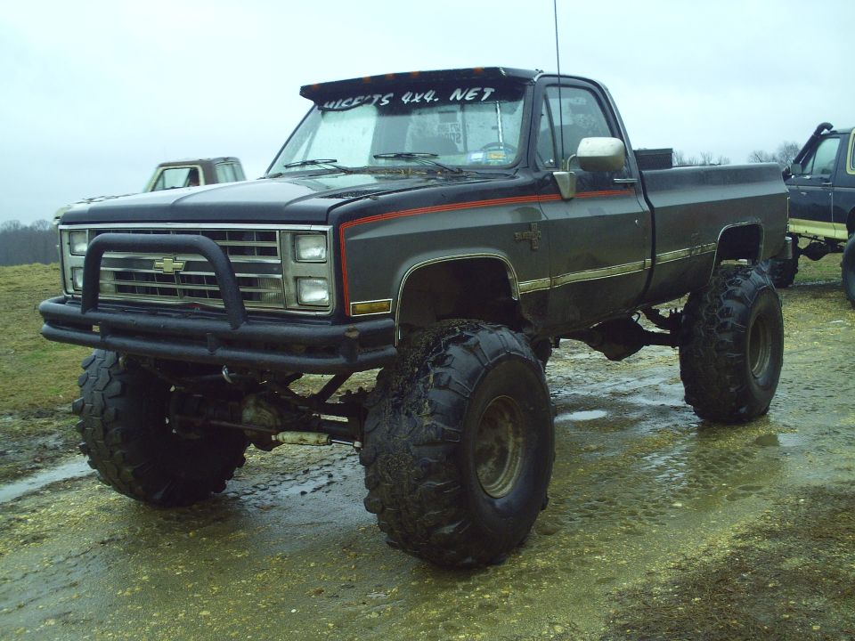 Dark gray lifted pickup truck with large off-road tires, bull bar, and red stripe detail