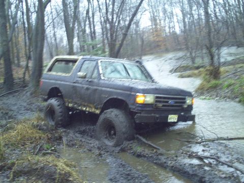 1990 Ford Bronco - Ford Bronco navigating a muddy trail through a wooded area.