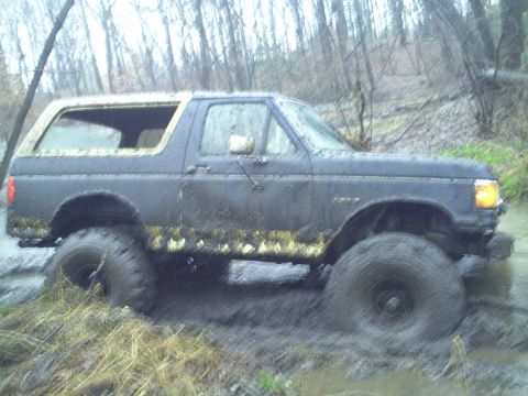 1990 Ford Bronco - This Ford Bronco is deep in the mud, with trees and brush surrounding it.