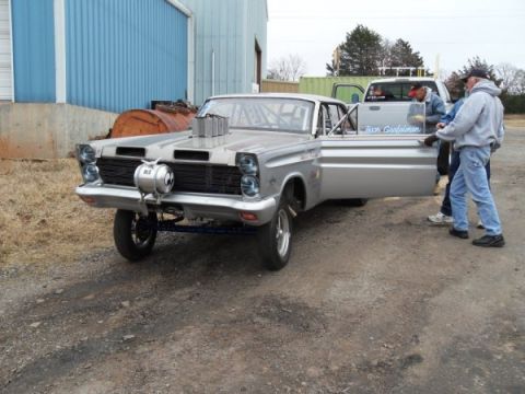 1963 Ford Fairlane - A modified 1965 Mercury Comet drag car is parked next to a pickup truck with people standing nearby.