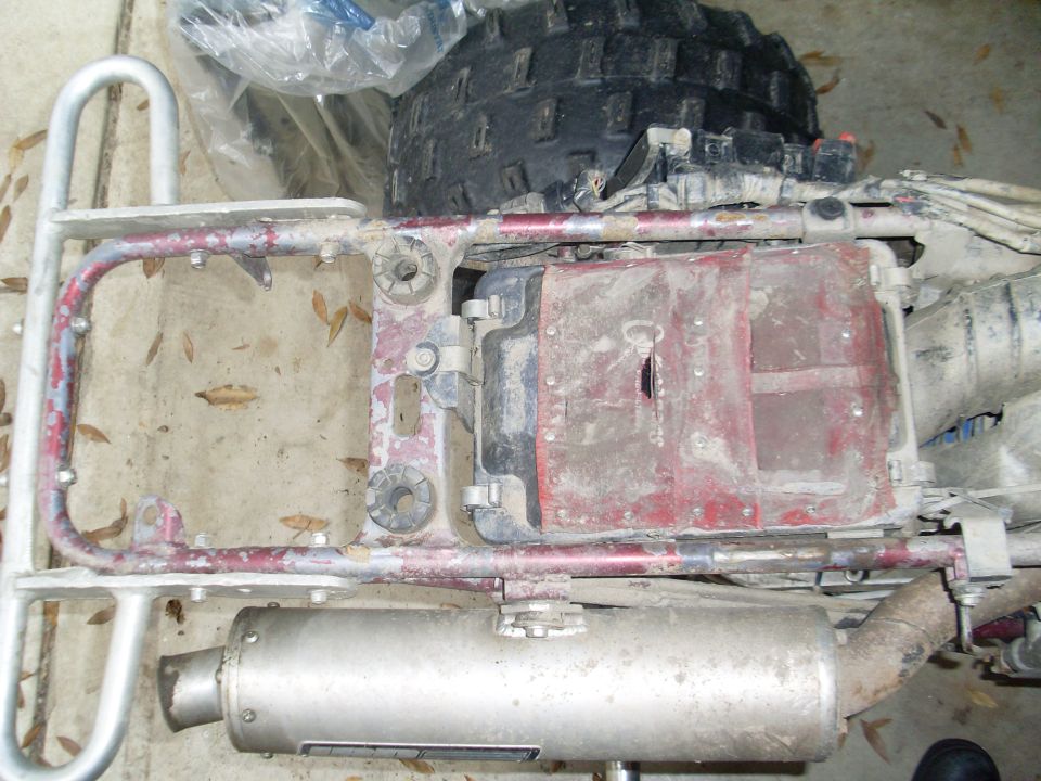 ATV frame with exhaust pipe and rear tire visible. Red plastic cover over engine components