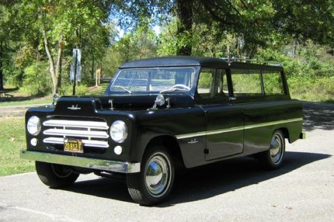 1991 Ford Bronco - Black vintage panel-style station wagon / carryall photographed from the 3/4 front on a paved lot with trees behind, showing a horizontal-b…