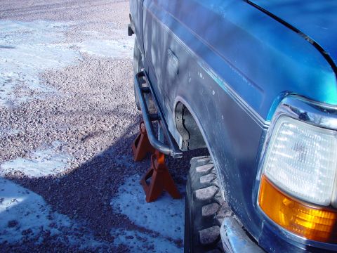 1993 Ford Bronco - A blue pickup truck is supported by orange jack stands, revealing its side step and wheel well.