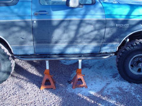 1993 Ford Bronco - A blue Ford Bronco is shown from the side, elevated on jack stands, with visible "BRONCO" badging.