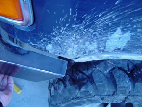 1993 Ford Bronco - A hand holds a metal part near the fender and tire of a blue vehicle covered in mud and ice.