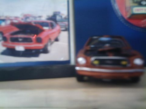 1978 Ford Mustang II - A toy car sits on a shelf in front of a framed photo of a red car.