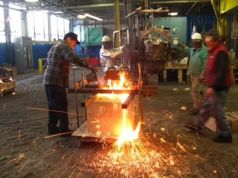 1972 Ford Ranchero - Molten metal being poured into a sand mold on a foundry floor, throwing a shower of orange sparks as a worker in a plaid shirt and ball cap…