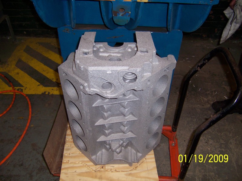 Aluminum engine block on wooden pallet, with orange cord and blue machinery in background