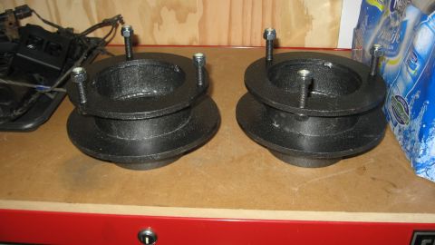 1997 Dodge 2500 - Two black suspension lift spacers are shown on a workbench, with a Supermotors logo visible.