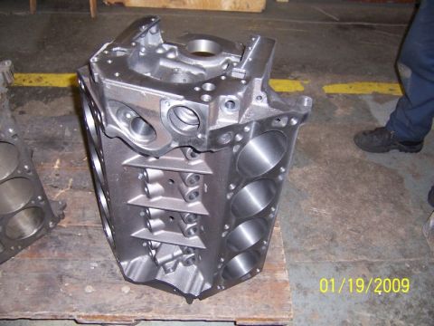 1972 Ford Ranchero - A bare V8 engine block stands upright on a wooden pallet in a machine shop, cleaned to bright bare metal with freshly honed cylinder bores…
