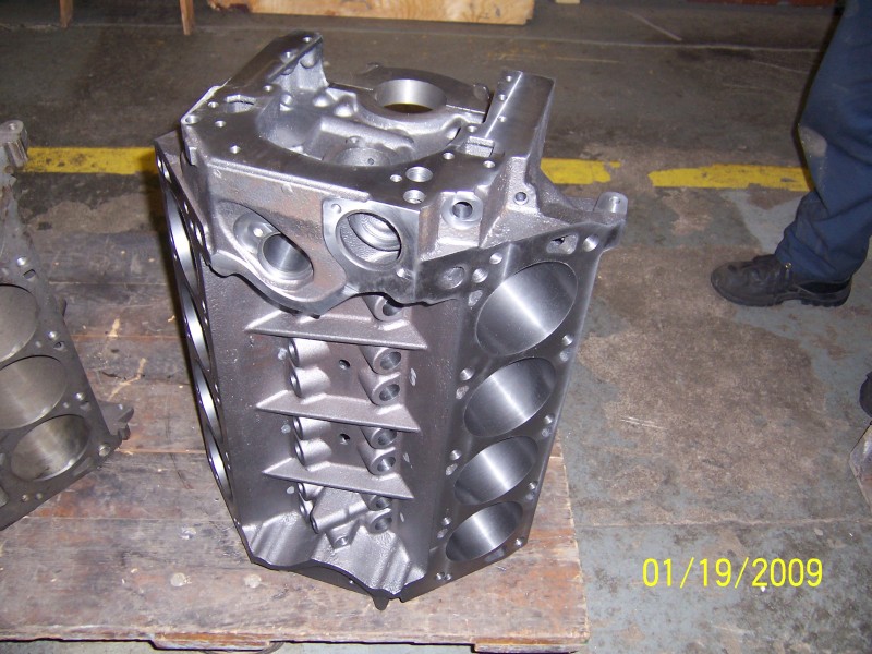 Cleaned bare V8 block upright on a pallet in a machine shop with honed bores visible