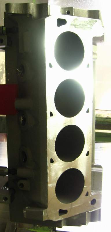 1972 Ford Ranchero - Close-up of one freshly decked cylinder bank on a V8 engine block clamped in a machine tool, showing four bright machined cylinder bores an…