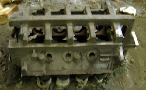 1972 Ford Ranchero - Rough as-cast V8 engine block lying in foundry sand immediately after shakeout, still gray with mold sand and unmachined. The open bottom s…