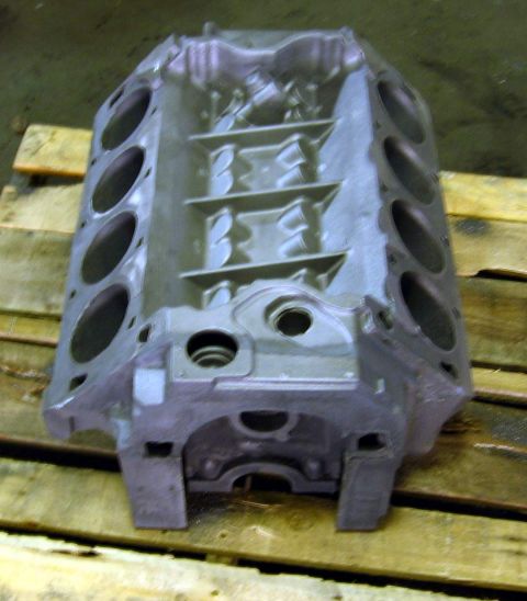1972 Ford Ranchero - A bare V8 cylinder block stands on end on a wooden pallet, freshly bead-blasted to a uniform gray, viewed down the lifter valley with all e…