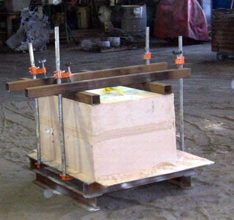 1972 Ford Ranchero - Assembled sand casting mold, a pink resin-bonded sand block clamped between steel plates with orange bar clamps and threaded rods, standing…
