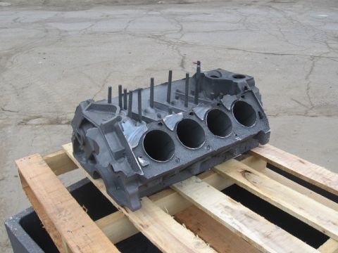 1972 Ford Ranchero - A rough as-cast iron V8 engine block lies on its side on a wooden pallet outdoors, showing four rough-cored cylinder bores on the exposed d…