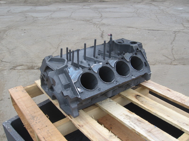 Rough as-cast iron V8 engine block on a pallet showing four cored cylinder bores