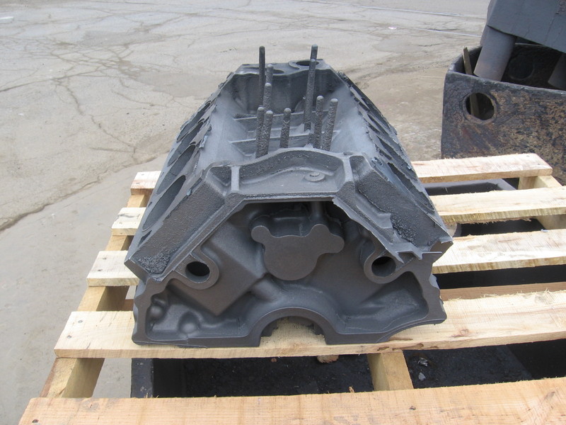 Raw unmachined iron V8 engine block casting on a wooden pallet outdoors