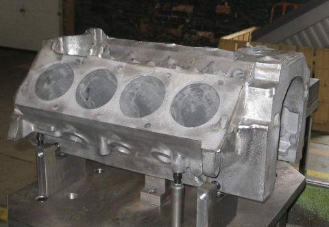 1972 Ford Ranchero - As-cast V8 engine block clamped on a machining fixture plate with locating pins and hold-down studs, tipped to show the rough-cast deck and…