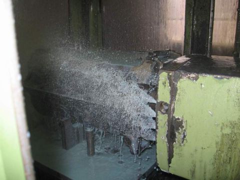1972 Ford Ranchero - Inside the enclosure of a green industrial milling machine as a cutter surfaces an engine block deck, with coolant spraying across the work…