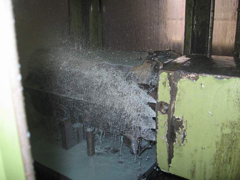 Engine block deck being milled inside a green machining center with coolant spraying over the cutter