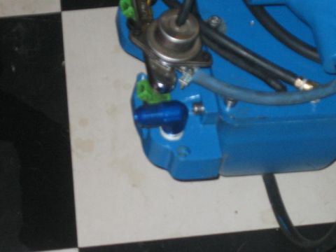 1996 Ford Thunderbird - Engine part with a blue fitting and hoses, photographed on a checkered floor.