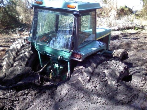 1990 Ford Bronco - A green tractor is deeply stuck in thick mud, with only its rear visible.