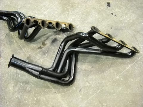 1978 Ford Bronco - Two black-painted long-tube V8 headers laid out on a concrete shop floor, the near one showing all four primary tubes running to a merge co…