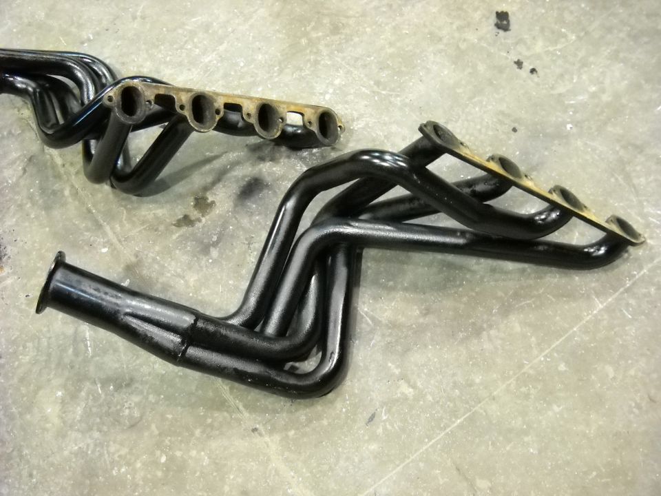 Two black long-tube V8 headers with collectors on a concrete shop floor