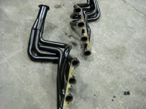 1978 Ford Bronco - A matched pair of black-painted long-tube V8 headers lying flange-up on a concrete shop floor, each with four primary tubes merging into a…